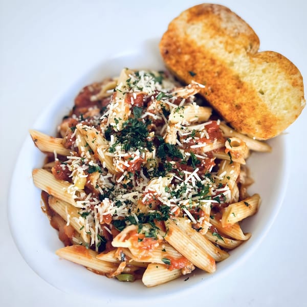 Penne pasta with red sauce, shredded cheese, and parsley, served with garlic bread.