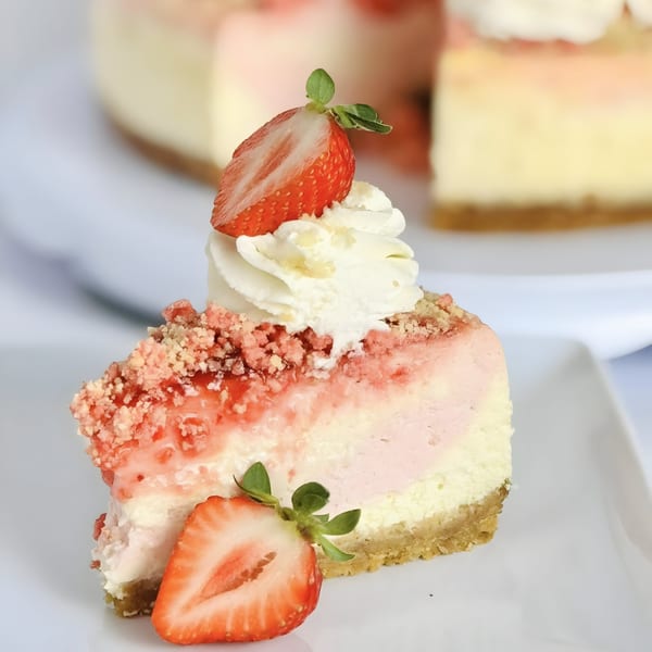 A slice of strawberry cheesecake with whipped cream and fresh strawberries on a white plate.