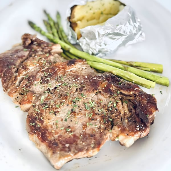 Grilled steak seasoned with herbs, served with green asparagus and a foil-wrapped baked potato.