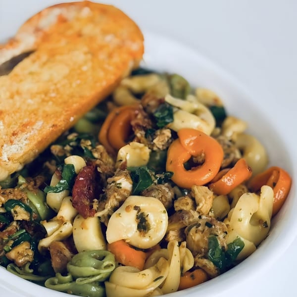 Colorful tortellini pasta with chicken, sun-dried tomatoes, and greens, served with garlic bread.