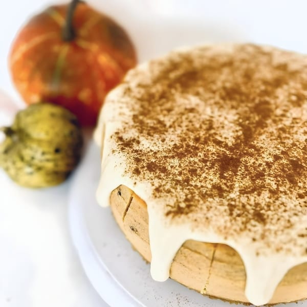 Pumpkin cheesecake with white frosting and cinnamon, next to two small gourds.
