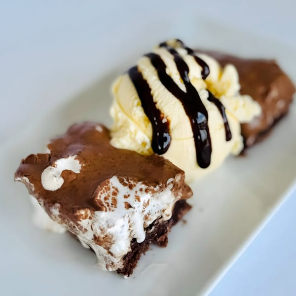 Two chocolate brownies topped with vanilla ice cream and chocolate syrup on a white plate.